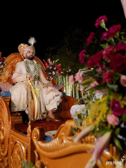 The groom awaits his bride, seated on a magnificent carved throne. The floral arrangements and lighting are designed to create a regal and anticipatory atmosphere.