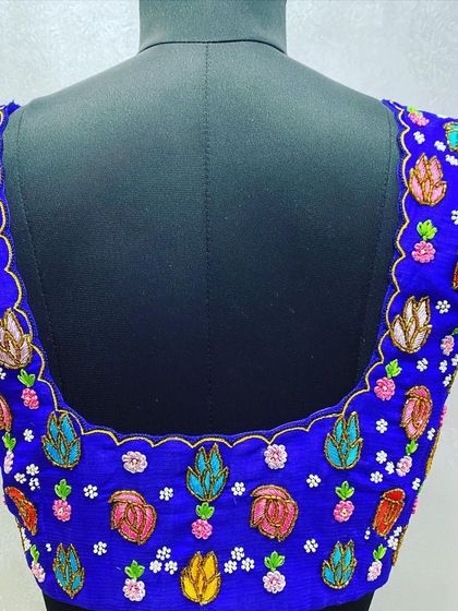 A royal blue blouse with colorful leaf and flower embroidery. The multi-color threadwork gives it a vibrant, playful look.