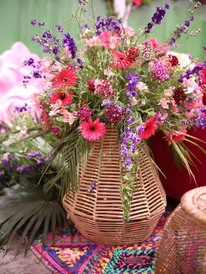 A vibrant bouquet of mixed flowers in a wicker vase. This arrangement combines pink gerberas, purple statice, and other colorful blooms, perfectly complementing a multi-hued mehndi theme.