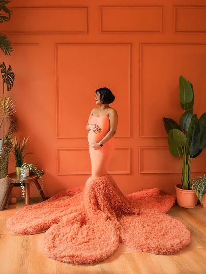 A bold and vibrant solo portrait. The rich orange tones and dramatic gown create a powerful image of a fierce mama-to-be.