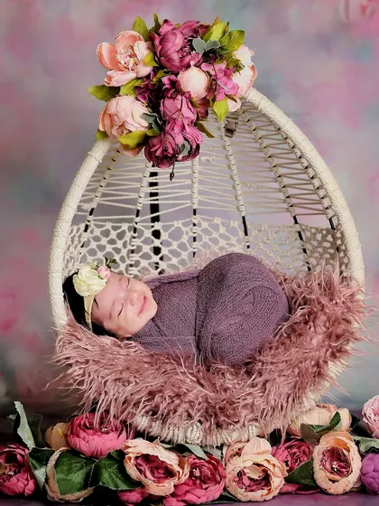 A sweet sleeping baby in a floral-themed setup. The purple wrap and surrounding peonies create a rich, colorful, and peaceful image.
