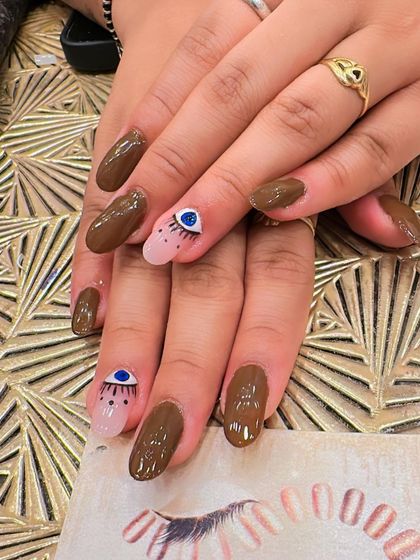 A chic and trendy design on brown oval nails. The accent nails feature a sheer base with a hand-painted evil eye design for a touch of mystique.