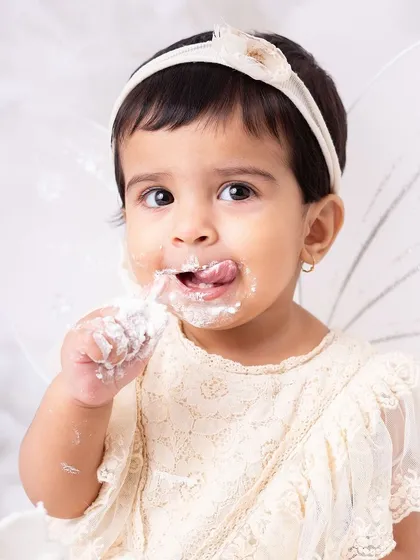 This little fairy is enjoying her cake with gusto. The "in the clouds" theme with angel wings creates a dreamy and ethereal vibe for a first birthday.