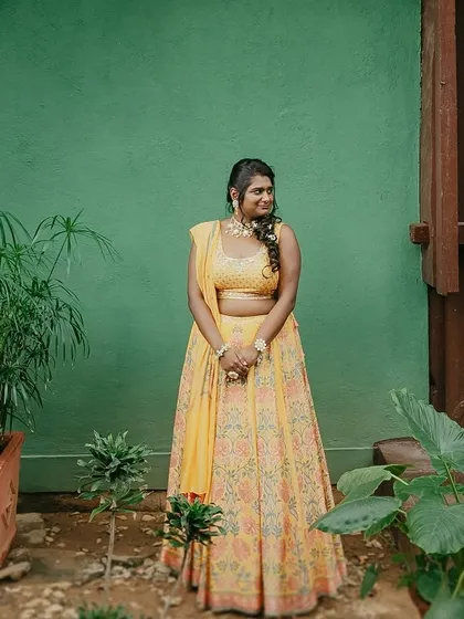 A bride in a yellow lehenga, laughing joyfully, a perfect candid moment captured in our gardens.