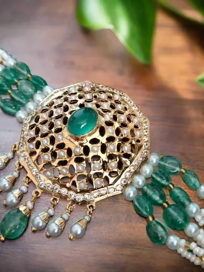 A detailed shot of the 'अमलतास' (Amaltas) choker. The intricate filigree work combined with pearls and green stones creates a truly luxurious feel.