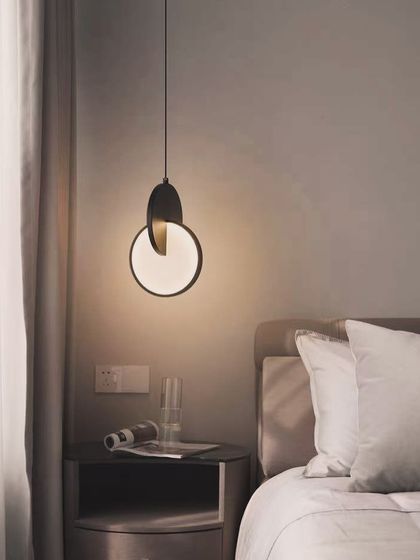A minimalist pendant light with an eclipse design, shown here as a chic bedside lamp.