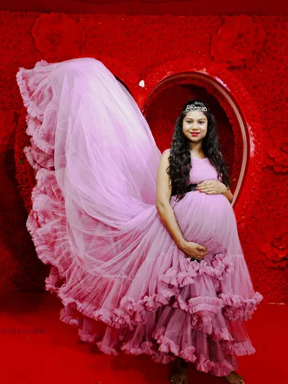 This dramatic maternity photo features a beautiful ruffled pink gown against a vibrant red heart backdrop in my studio. The long train creates a stunning visual effect.