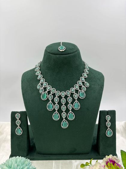 An elegant AD necklace set with a matching maang tikka. The cascading design with teardrop stones is available in green, pink, and all-white, perfect for receptions and parties.