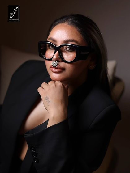 A bold and confident close-up portrait. The oversized glasses, nose ring, and direct gaze create a powerful statement look.