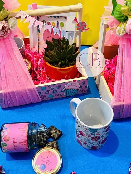 A detailed view of our luxurious candy-themed first birthday return favours. This image shows the custom-printed mug and jar of treats next to the beautifully decorated pinewood basket.