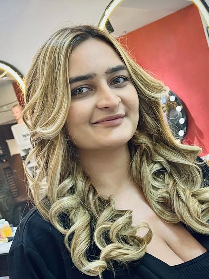 A happy client showing off her new blonde curls. The color is vibrant, and the hair looks healthy and full of bounce, thanks to our premium products and expert application.