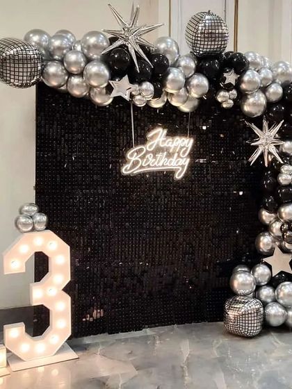 A rockstar-themed setup for a 13th birthday. The black sequin wall, silver and black balloons, disco balls, and star-shaped foils come together to create a cool, edgy, and fun party vibe.