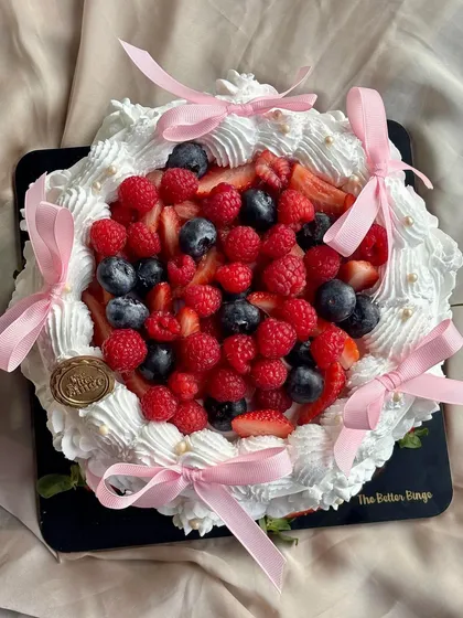 A timeless classic, my Vanilla and Berries cake is light, fresh, and beautiful. It features a fluffy vanilla sponge topped with a mountain of fresh, seasonal berries and delicate pink bows.