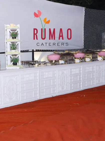 A clean and professional buffet setup featuring our "Rumao Caterers" branding. The white counters and pink chafing dishes can be customized to match your event's color scheme.