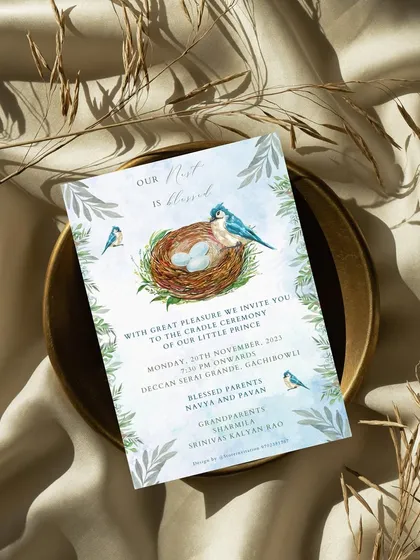 A beautiful shot of the "Nest is Blessed" cradle ceremony invitation, styled on a bed of silk. The watercolor design with the bird's nest and delicate leaves looks truly elegant and special.