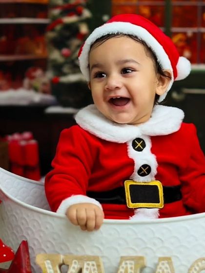 A happy baby Santa enjoying our cozy Christmas set, complete with festive props and a warm, glowing background.