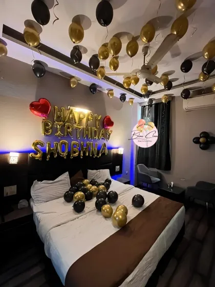 A romantic bedroom decoration for a birthday, with black and gold balloons on the ceiling and bed.