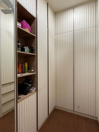 This walk-in closet is designed for maximum storage and style. The wardrobe shutters feature a curved fluting design in a soft off-white PU finish, with an open shelving unit for easy access to everyday items.