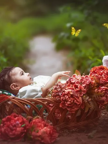 A six-month-old baby lies peacefully in a basket filled with flowers on a rustic path, watching butterflies flutter by. A perfect blend of nature and innocence.