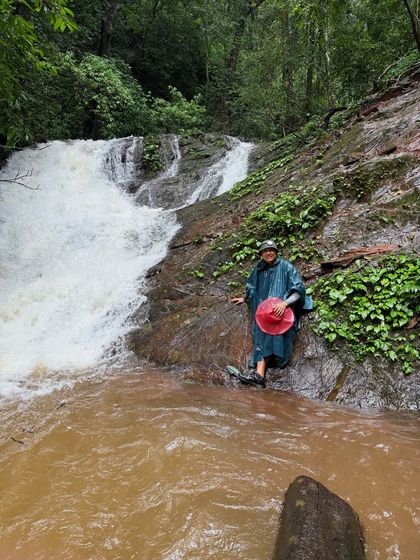 A trekker in a poncho enjoying a quiet moment by a stream.