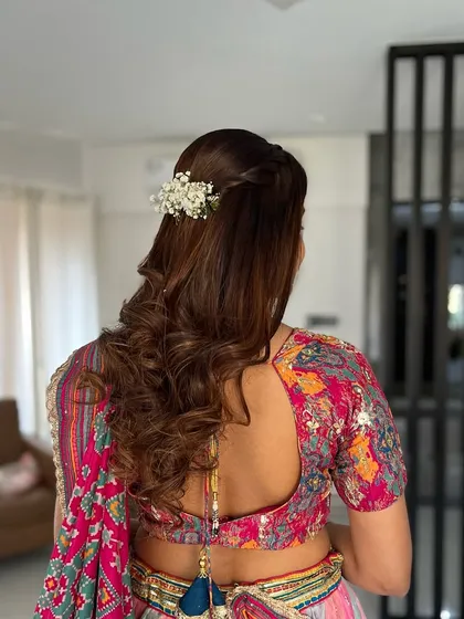 A perfect blend of elegance and charm for an engagement day. This half-up hairstyle features soft curls and is adorned with a simple gajra.