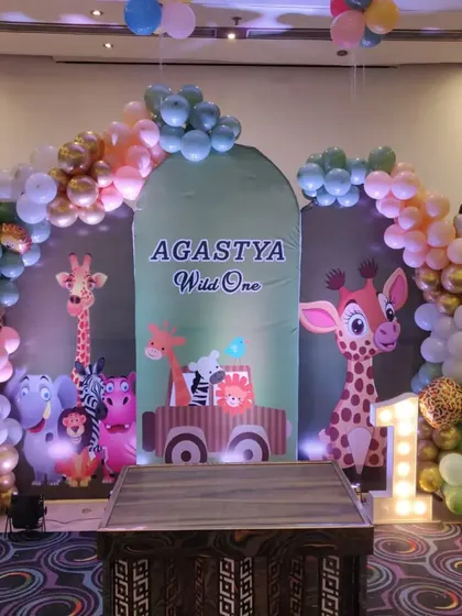 A "Wild One" jungle theme for a first birthday. This setup includes a large backdrop with cartoon animals, a balloon arch, and a marquee number '1'.