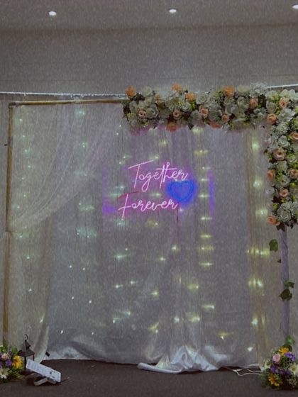 An elegant and minimalist reception backdrop with a 'Together Forever' neon sign and a floral arrangement.