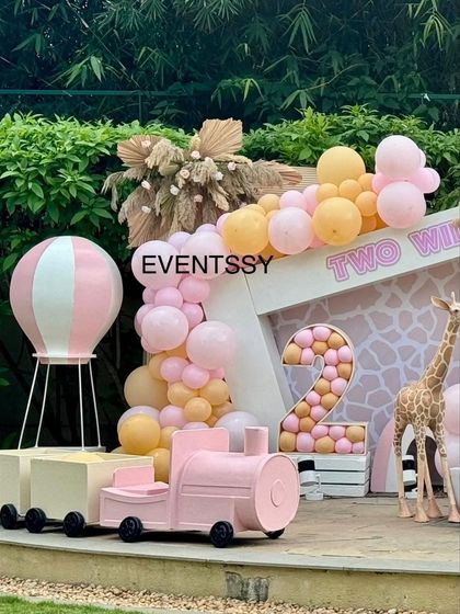 A "Two Wild" birthday party with a pastel and pink jungle theme. This softer take on a jungle party uses a pink train, a hot air balloon, and a giraffe prop for a sweet and adventurous feel.