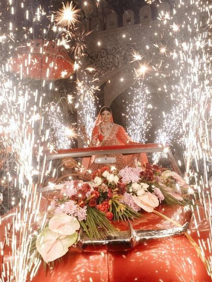 The full view of the bride's spectacular entry in a vintage car, surrounded by cold pyrotechnics. This is end-to-end execution of a high-impact concept.