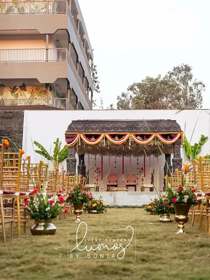 A wide view of a temple-style mandap setup in a garden, showcasing the grandeur of the architecture and the surrounding landscape.