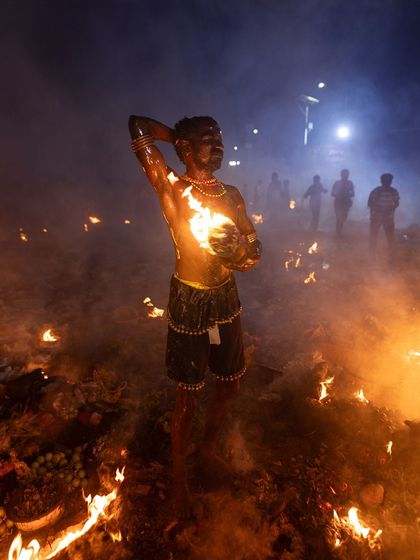A wider perspective of a devotee amidst the fires of the Kulasai festival, capturing the scale and intensity of the nighttime ceremony.