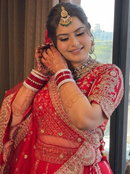 The final touches. Jagriti adjusts her earring, giving a glimpse of the complete look with her intricate henna and stunning jewelry, all tied together with a classic makeup application.