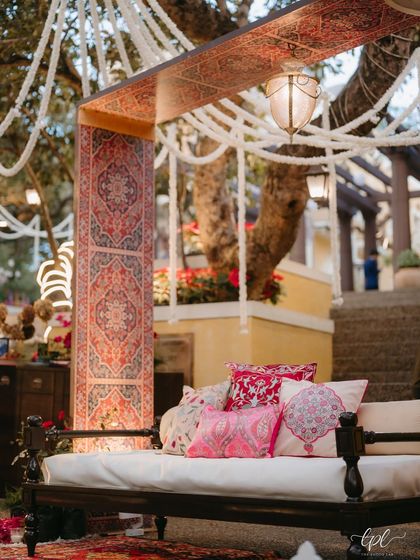 A cozy seating nook from a Kashmiri Sufi themed Mehfil. The design featured a traditional diwan, rich textiles, bolster cushions with intricate patterns, and hanging floral strings.
