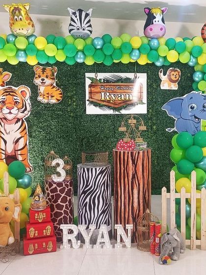A vibrant jungle theme for a third birthday, with a focus on tigers and zebras. The setup includes a green backdrop, animal-print plinths, and lots of plush and cutout animals to complete the scene.
