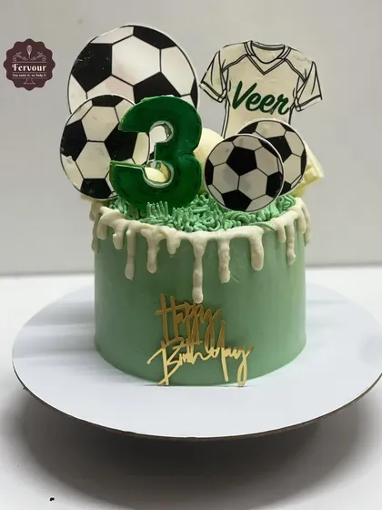 A football theme cake with a green drip design. This cake is topped with edible footballs and a jersey, making it a great choice for a 3rd birthday party.