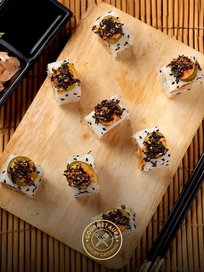 A wooden board displays pieces of sushi topped with a savory crumble and jalapeño slices, offering a unique combination of textures and a hint of spice.