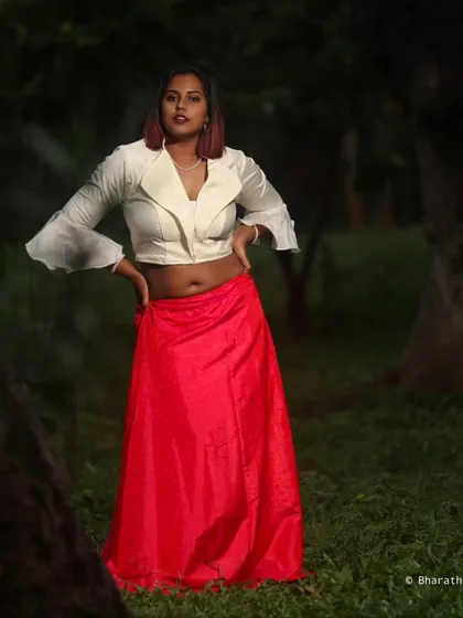 A powerful, confident pose in the white top and pink skirt. The lighting highlights the model's form and the texture of the fabrics.