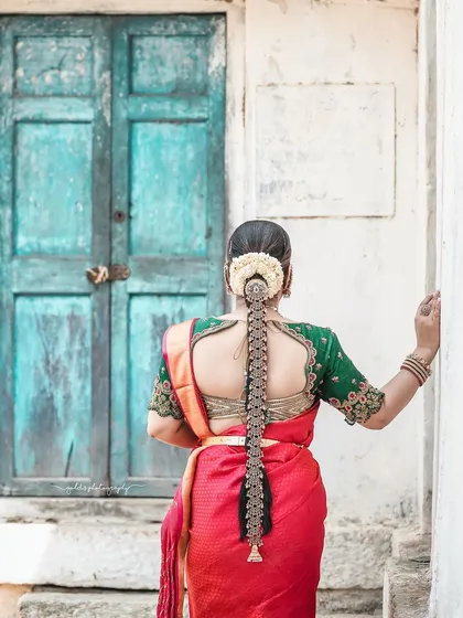 A beautiful shot from behind, highlighting the intricate bridal hairstyle and the stunning embroidery on the blouse, set against a rustic blue door.