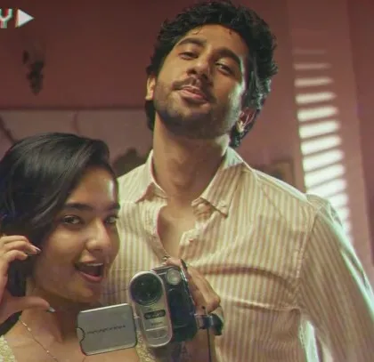 A playful scene from the film, captured with a retro camcorder effect. The styling reflects a youthful and fun-loving couple, with casual, comfortable outfits that feel genuine and lived-in.