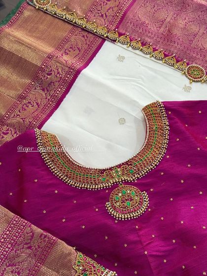 This blouse features a necklace-like embroidery pattern around the neckline, complete with a pendant design. It's crafted with green and red stones, giving the illusion of wearing a real temple jewellery set.