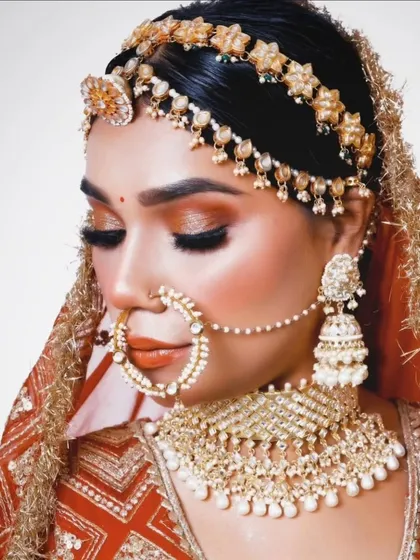 This bride is adorned in a classic gold and pearl jewellery set. The look includes a floral matha patti, a detailed choker, and a traditional nath, perfect for a timeless wedding look.