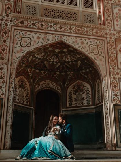 A couple shares a laugh while seated in an ornate archway, with intricate floral patterns creating a rich, textured background. This shot showcases the vibrant colors and detailed architecture of Rajasthani palaces.