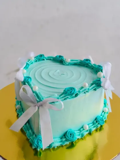 This lovely heart-shaped cake was made for a bridal shower. The light blue frosting is accented with white ribbons and pearls, creating a delicate and celebratory look.