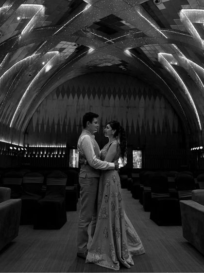 A classic black and white portrait in a grand, atmospheric hall. The symmetry of the room and the couple's central placement create a powerful and timeless image.