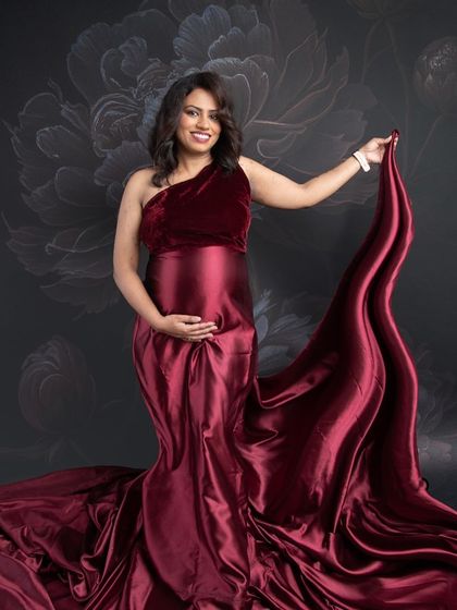 A confident and beautiful pose in a one-shoulder velvet and satin gown. The flowing fabric and the floral backdrop create a sophisticated and artistic portrait.