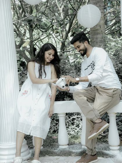 A cute moment where the groom shows the bride a picture on a polaroid camera, set in a beautiful garden gazebo.