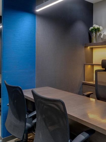 Private cabins in the Pharmaserve office use a bold blue textured wallpaper to create a distinct and professional look. The warm wood tones of the desk and shelving provide a sophisticated contrast.
