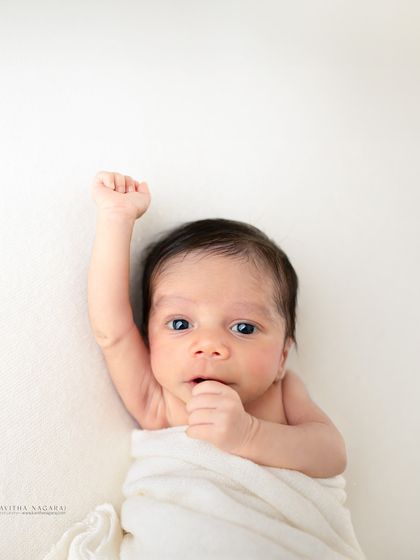 A two-week-old baby raises a fist, looking ready to take on the world. This minimalist portrait on a white background is full of personality.
