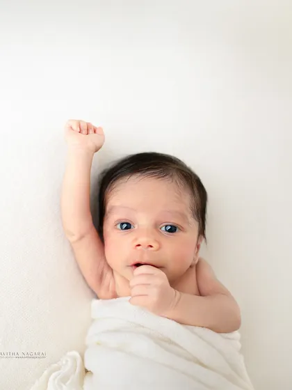 A two-week-old baby raises a fist, looking ready to take on the world. This minimalist portrait on a white background is full of personality.