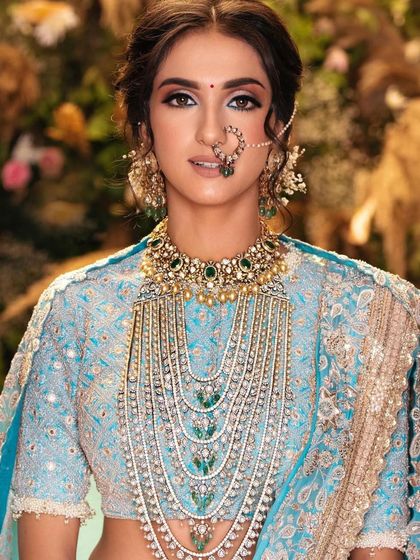 A close-up of the pastel blue bridal look, showing the intricate detail of the makeup and the stunning layered necklace. The skin is kept luminous and fresh.
